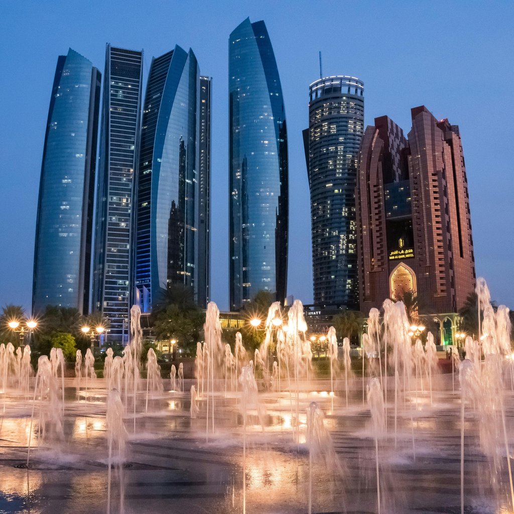 View of Abu Dhabi's skyline with illuminated fountains at twilight, showcasing modern architecture.