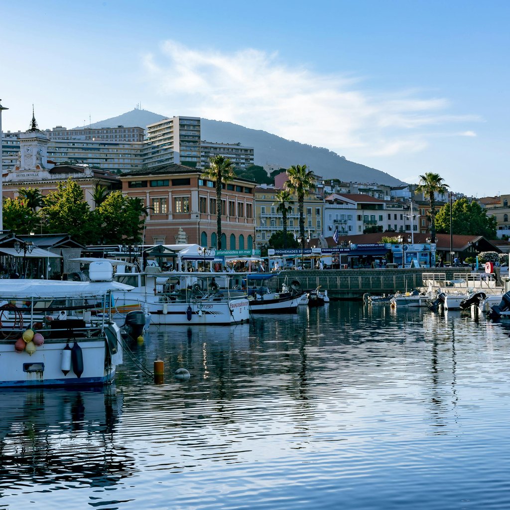 Peaceful harbor in Ajaccio, Corsica with moored boats reflecting cityscape and mountain backdrop.
