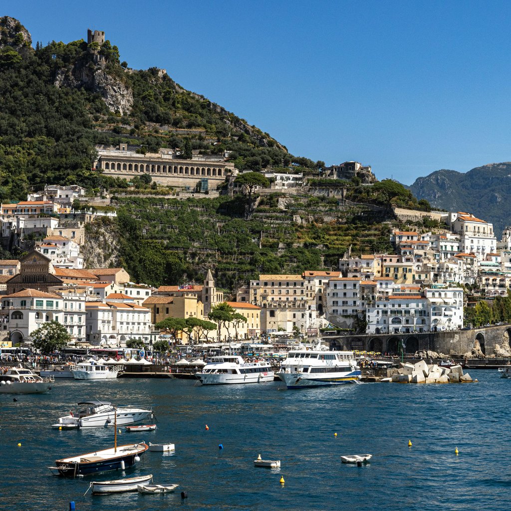 Breathtaking view of Amalfi's coastal town and marina under a clear summer sky in Italy.