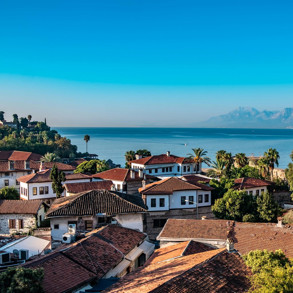 Captivating view of Antalya's coastline with traditional houses, vivid blue sea, and distant mountains.