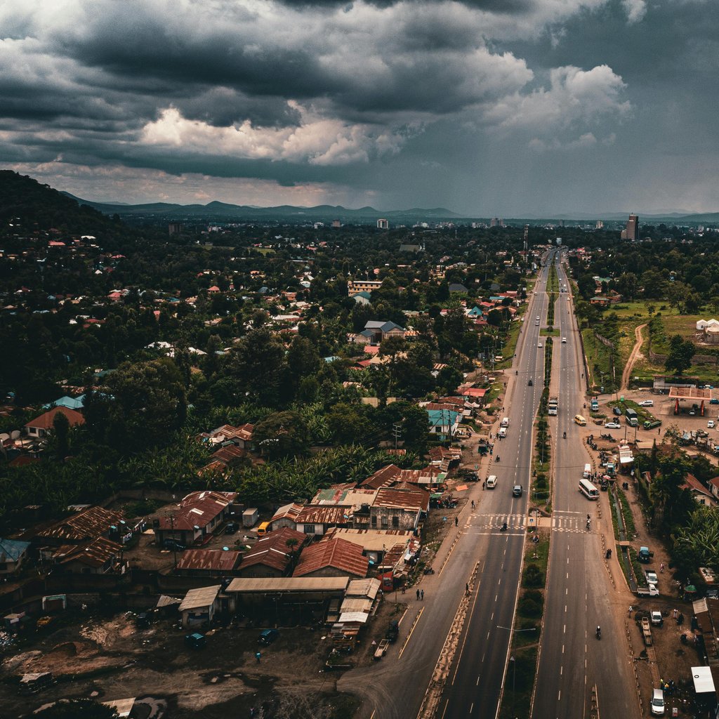Aerial view of a main road in Arusha, Tanzania, with overcast skies and surrounding greenery.