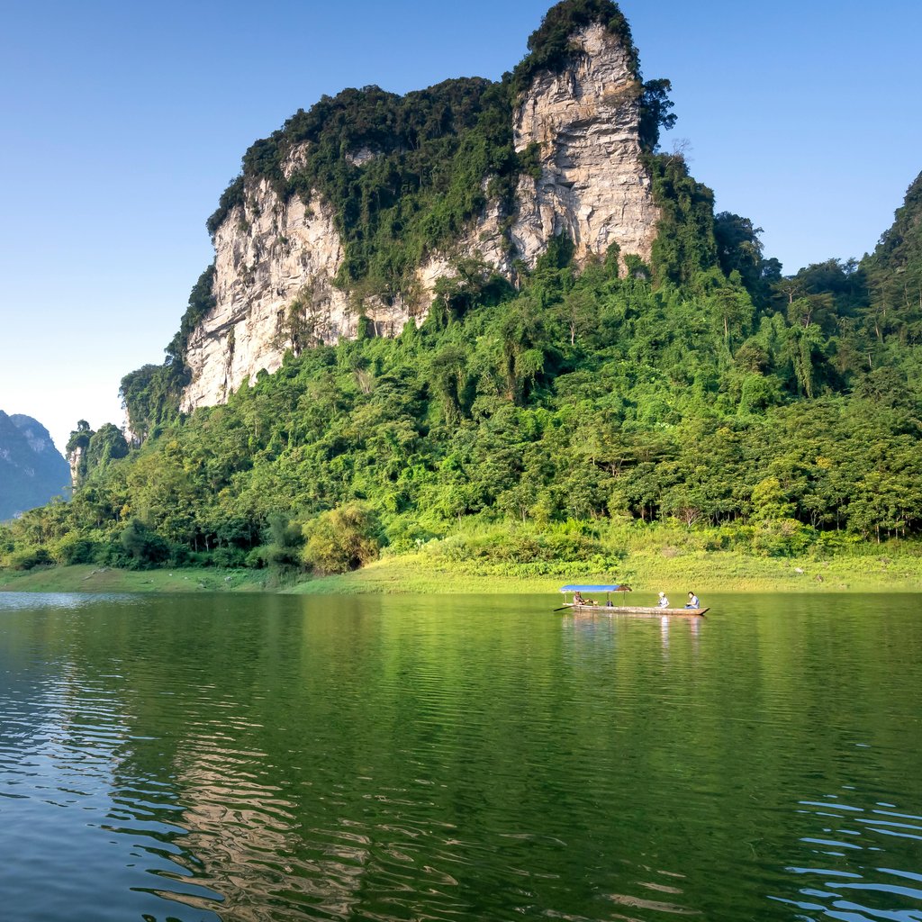 Idyllic landscape of a lush mountain with calm lake reflection under a clear blue sky.