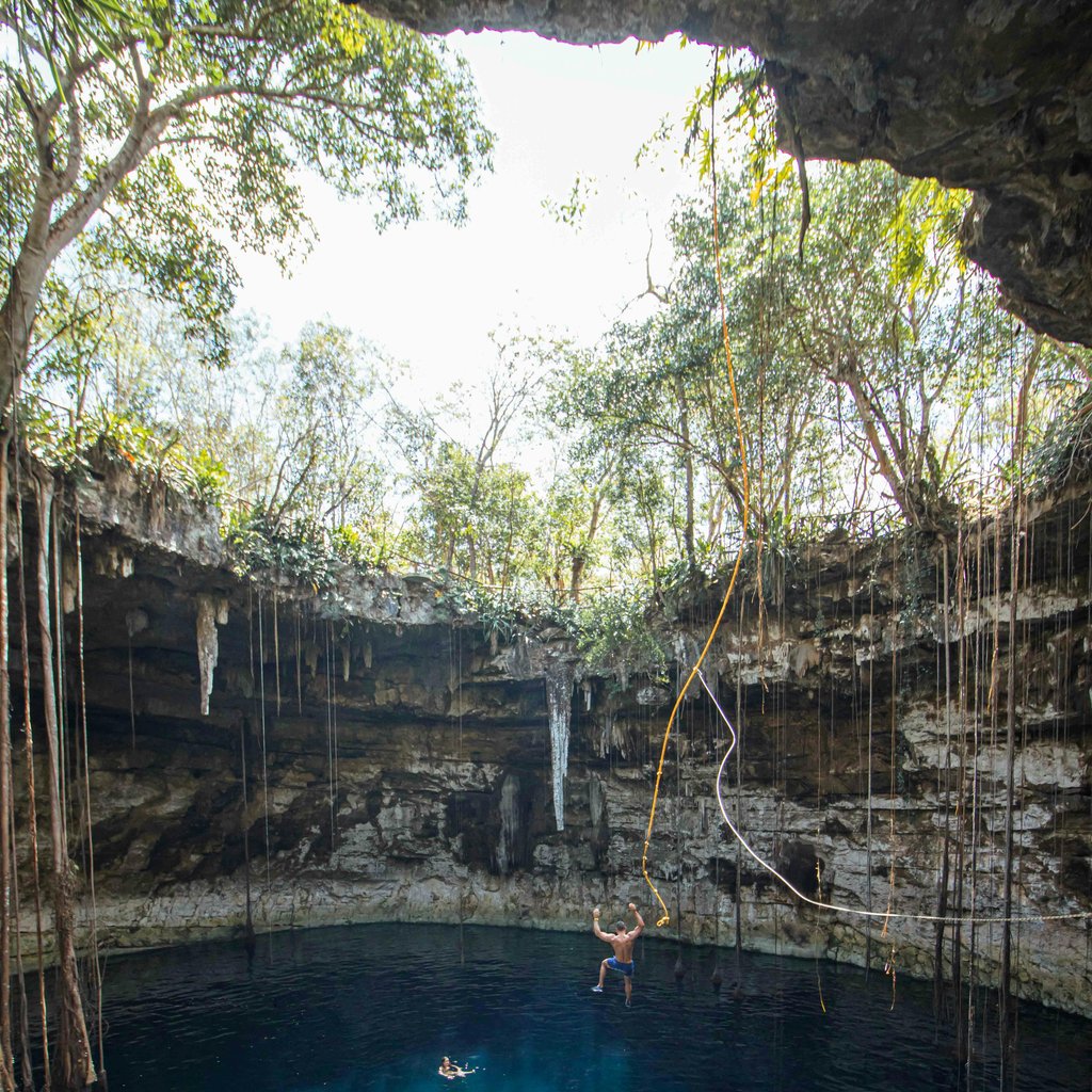 Adults swimming in a clear cenote with blue water and lush greenery in Halatun, Mexico.