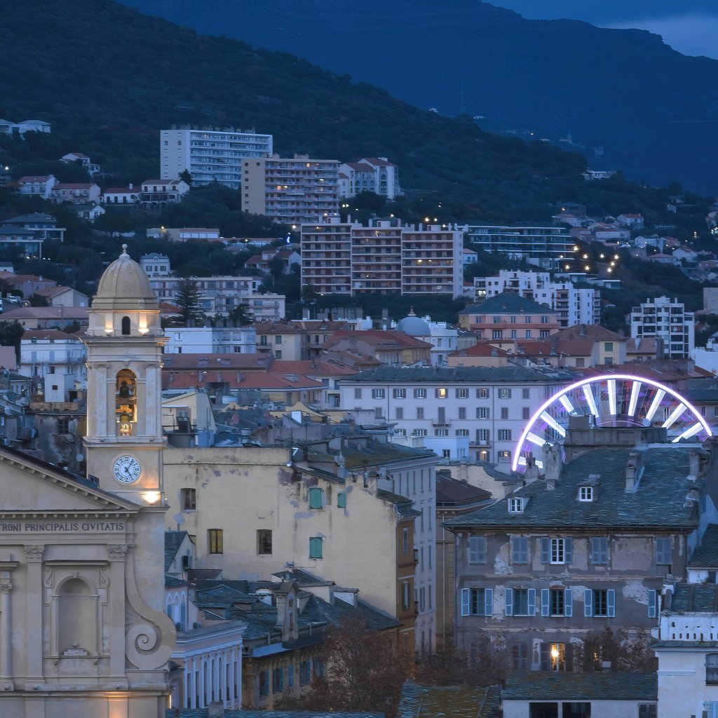 A scenic nighttime view of Bastia, Corse, France featuring a Ferris wheel and illuminated church.