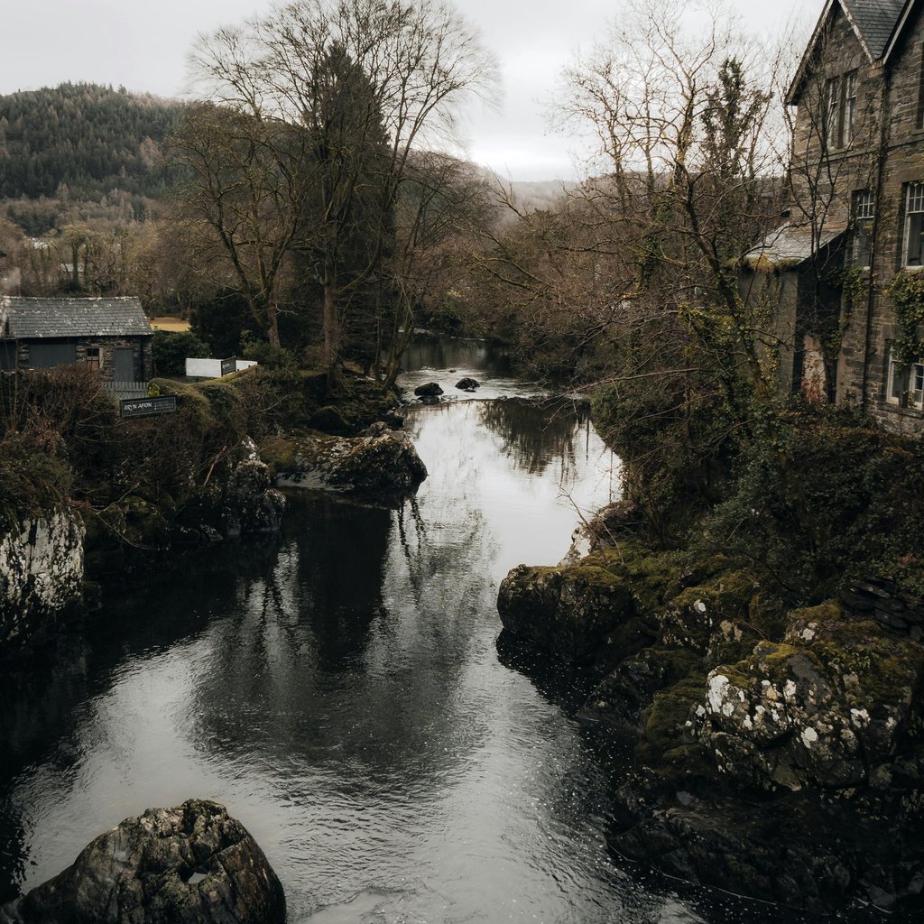 Scenic view of a river flowing through Betws-y-Coed, Wales, showcasing classic architecture and natural beauty.
