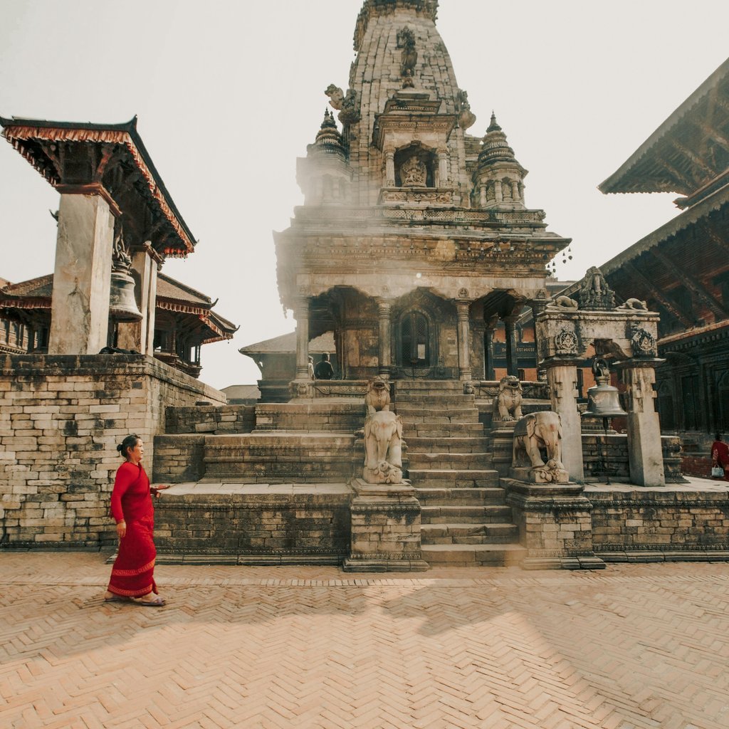 A woman in a red sari walks past ancient architecture at Bhaktapur Durbar Square, a UNESCO World Heritage Site in Nepal.