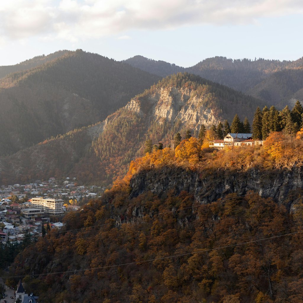 A picturesque mountain valley with autumn foliage in Georgia, highlighting a tranquil village under sunlight.