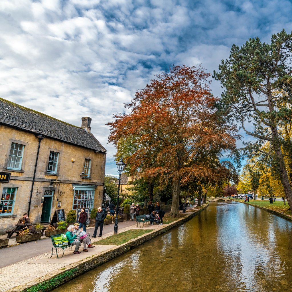 Charming autumn view of Bourton-on-the-Water with a tranquil stream and vibrant foliage.