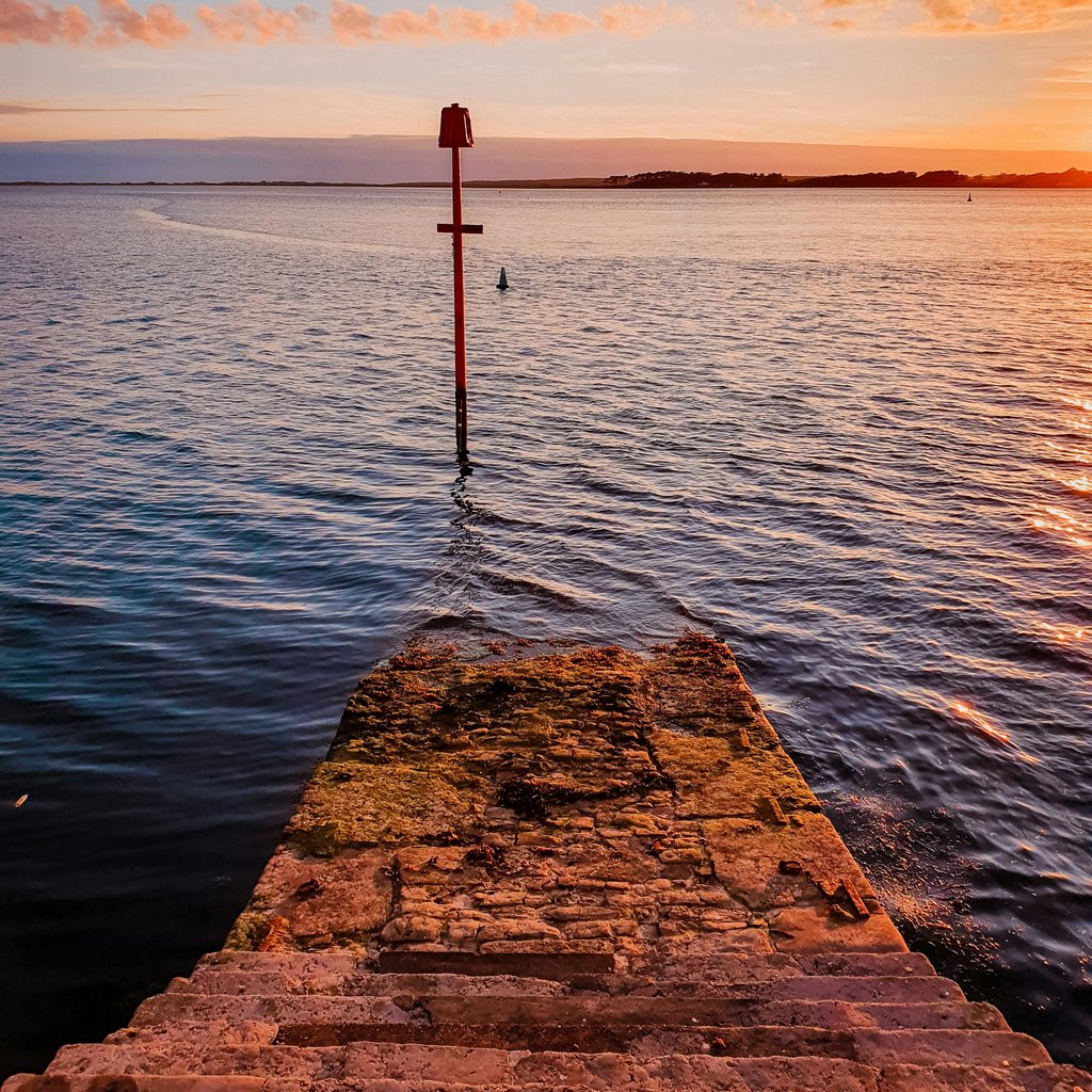 Tranquil sunset view over the coastline in Caernarfon, Wales with navigational aid and sea steps.