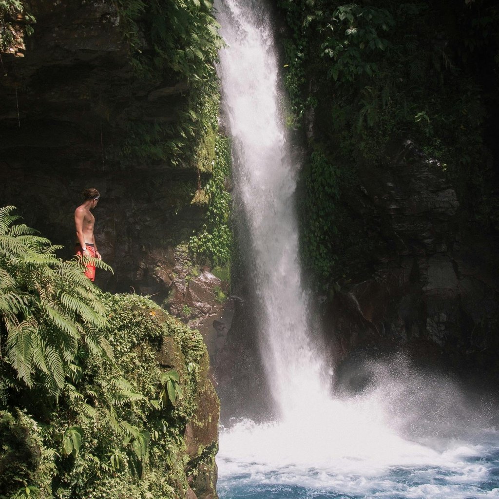 A man stands by a lush waterfall in Northern Mindanao, Philippines, amidst vibrant greenery.