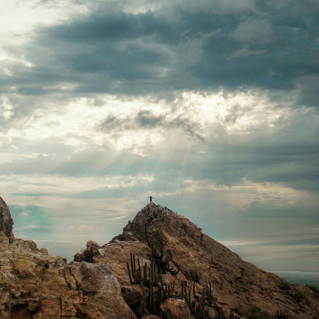 A rocky mountain with a visible cross at the peak under an overcast sky in Chiclayo, Peru.