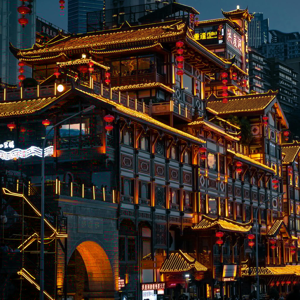 Night view of illuminated traditional Chinese architecture in Chongqing's urban setting.