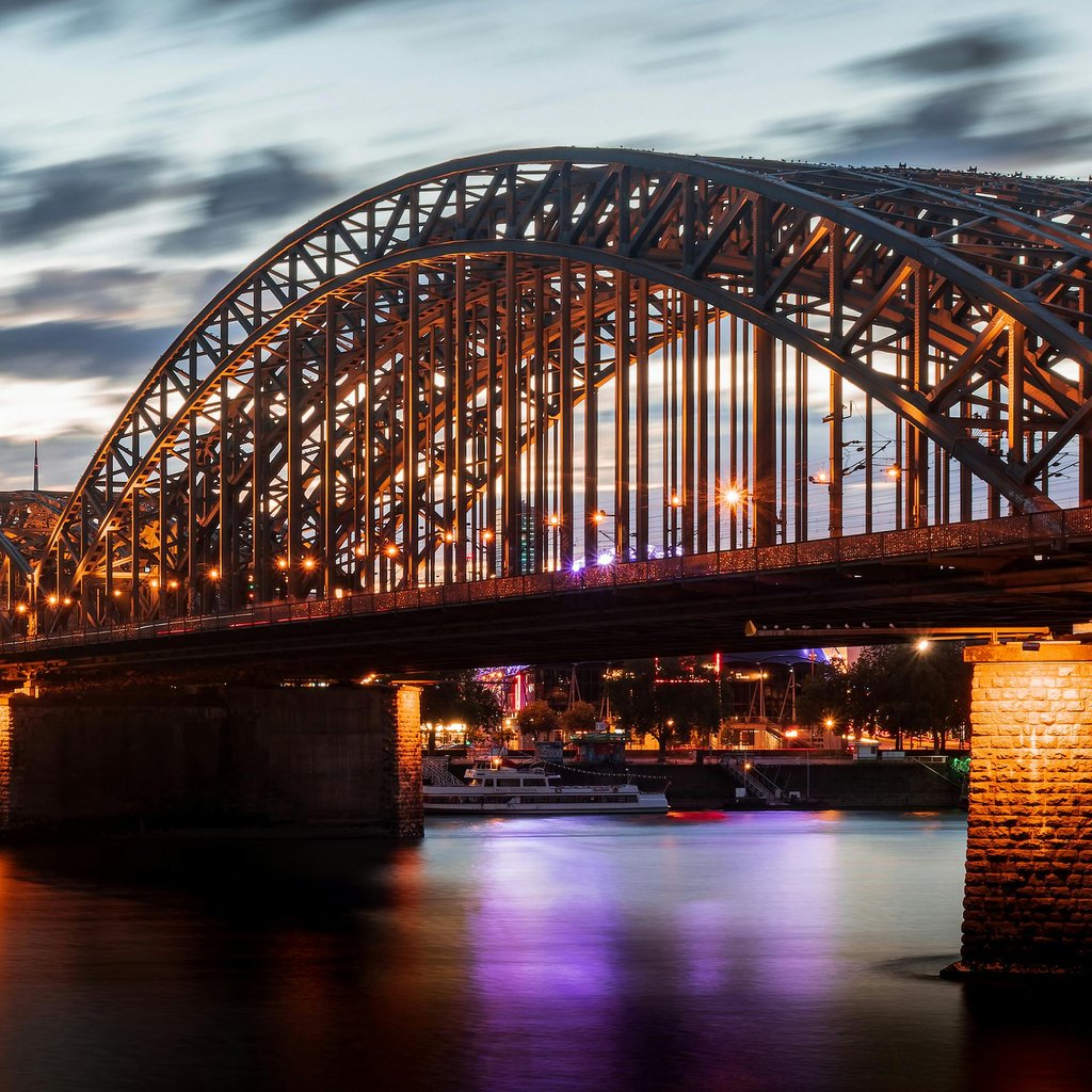 Stunning view of Cologne Cathedral and Hohenzollern Bridge illuminated at dusk over the Rhine River.