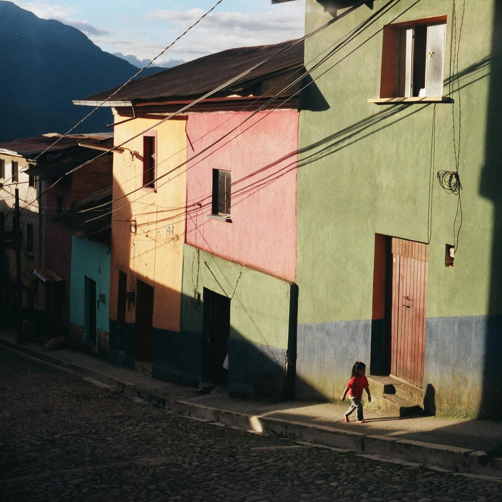 A child walks along colorful houses in Coroico, Bolivia, under sunlight.