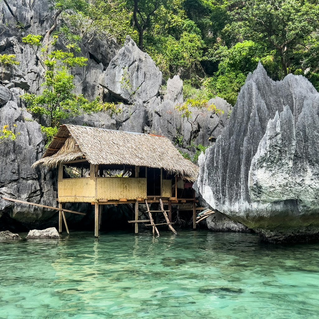 Tranquil bamboo hut by clear waters amidst limestone cliffs in Coron, Philippines.