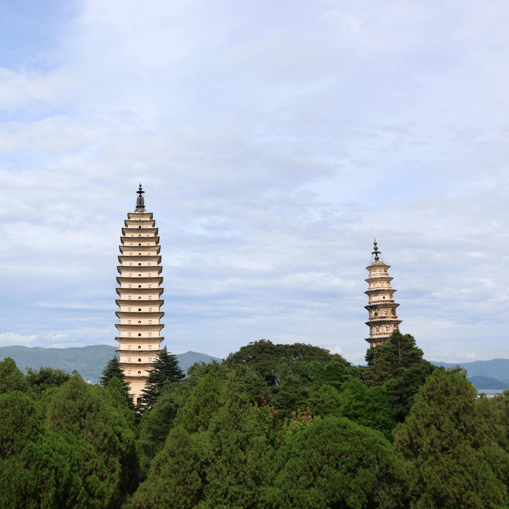 Elegant view of the Three Pagodas in Dali, China, framed by lush greenery and distant mountains.