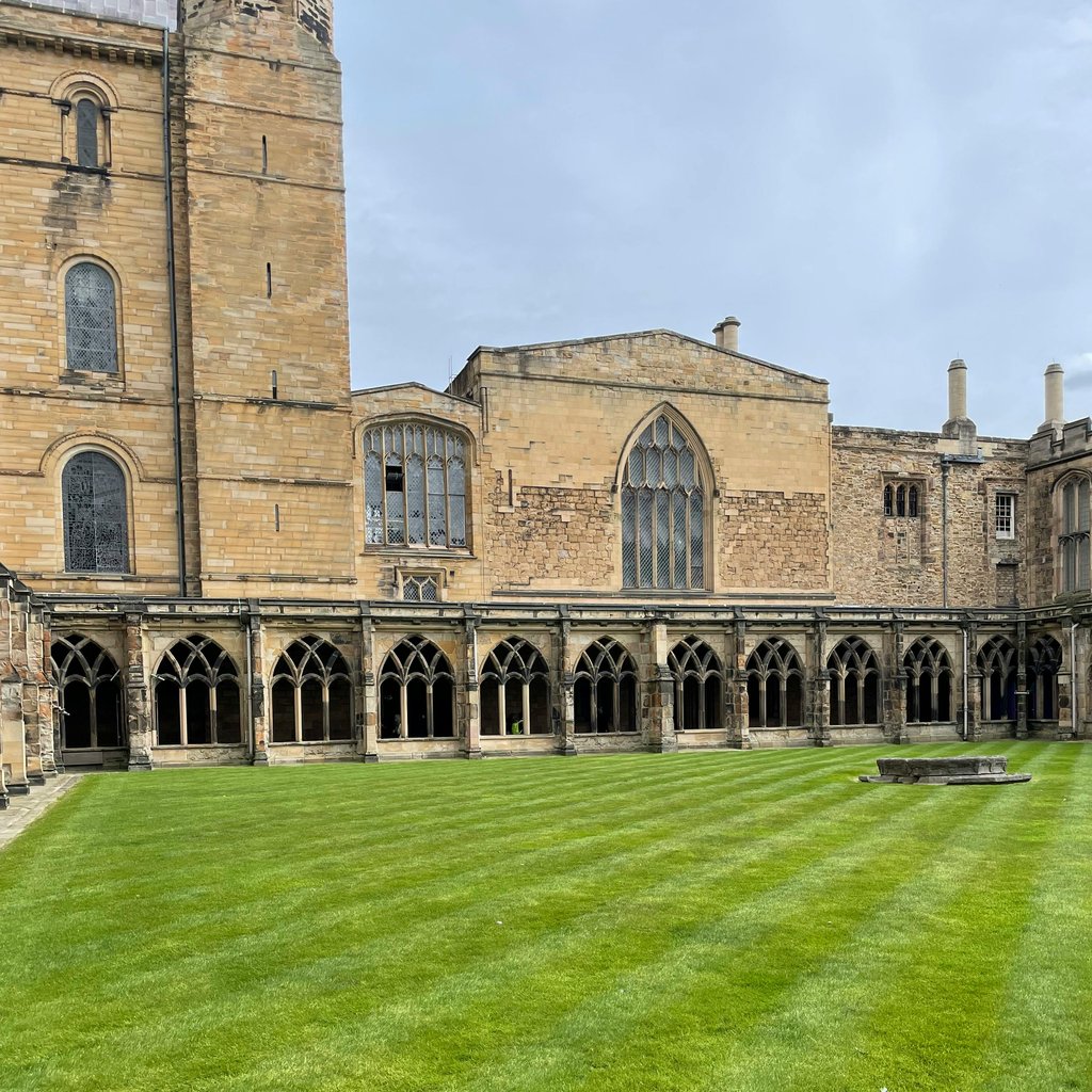 A serene view of Durham Cathedral's cloister, showcasing historic architecture and lush grass.