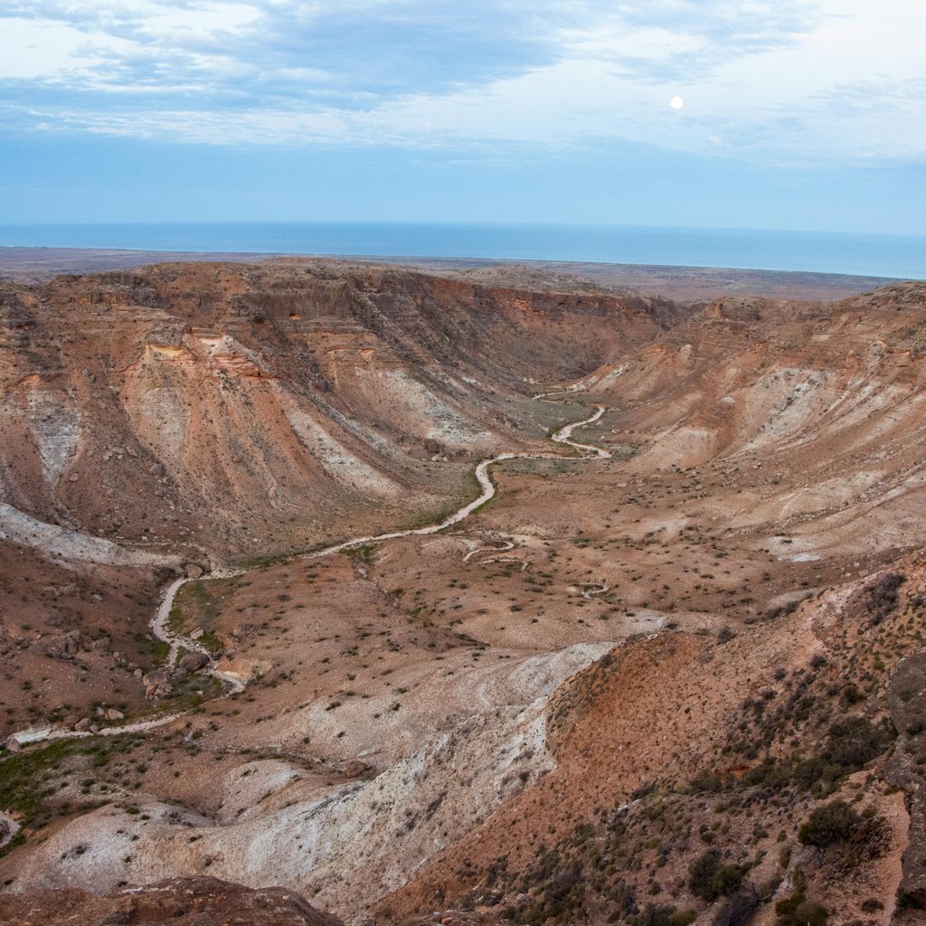 Wide view of Exmouth canyons at dusk with moonrise and geological formations.