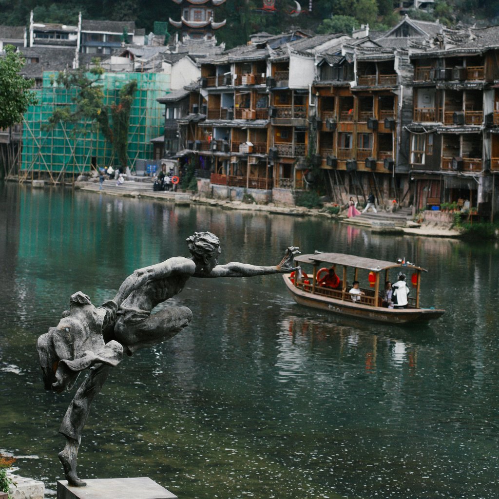 Scenic view of a historic Chinese river town with a river sculpture and boat.