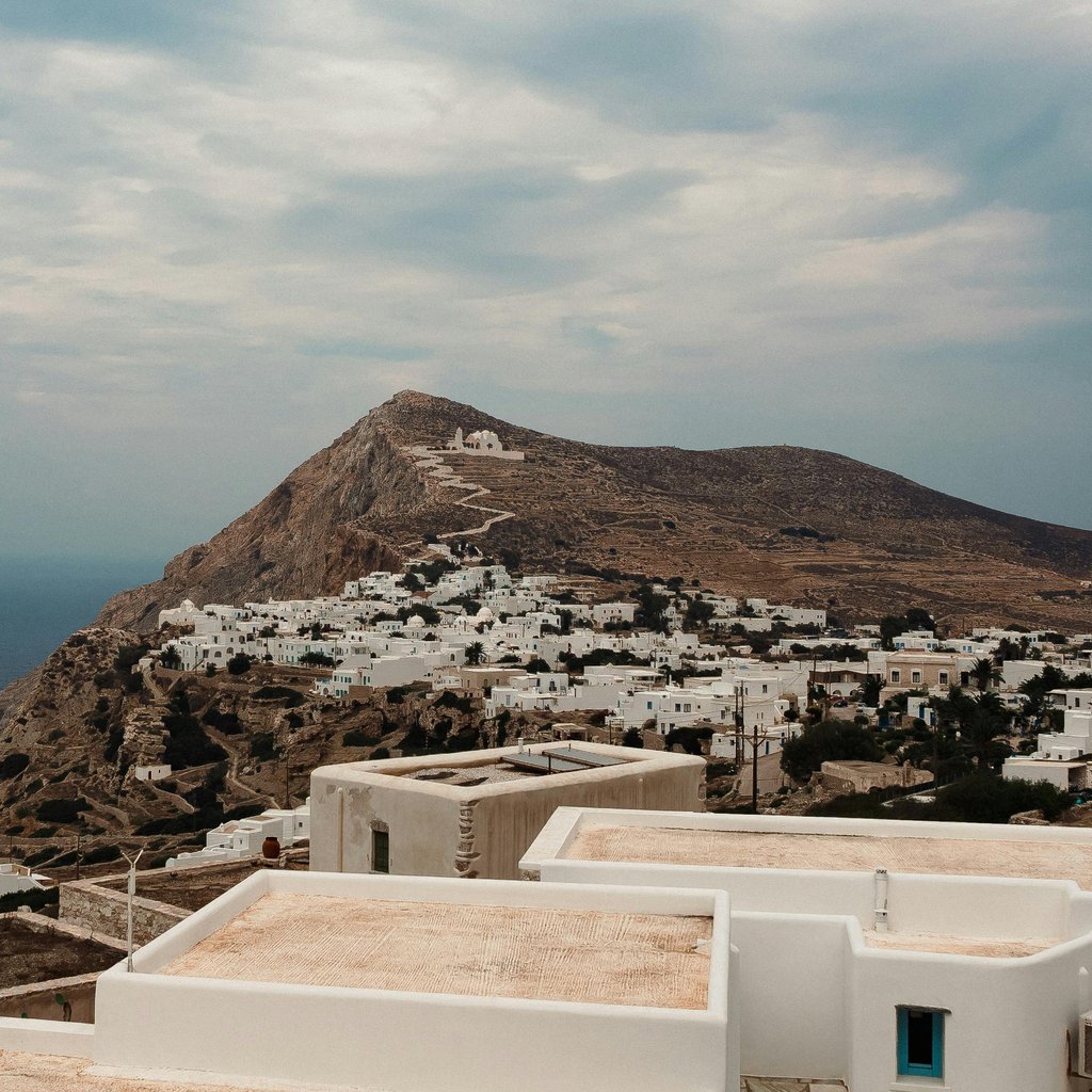 Capture of a beautiful white village atop a rugged cliff in Folegandros, Greece with the sea in the background.
