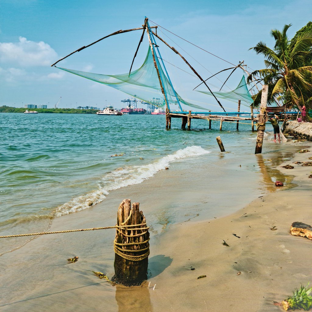 Explore picturesque Fort Kochi beach with traditional Chinese fishing nets against a blue sky.