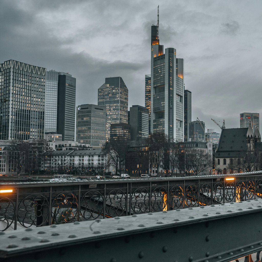 Frankfurt's modern skyline and iconic bridge under a moody, overcast sky.