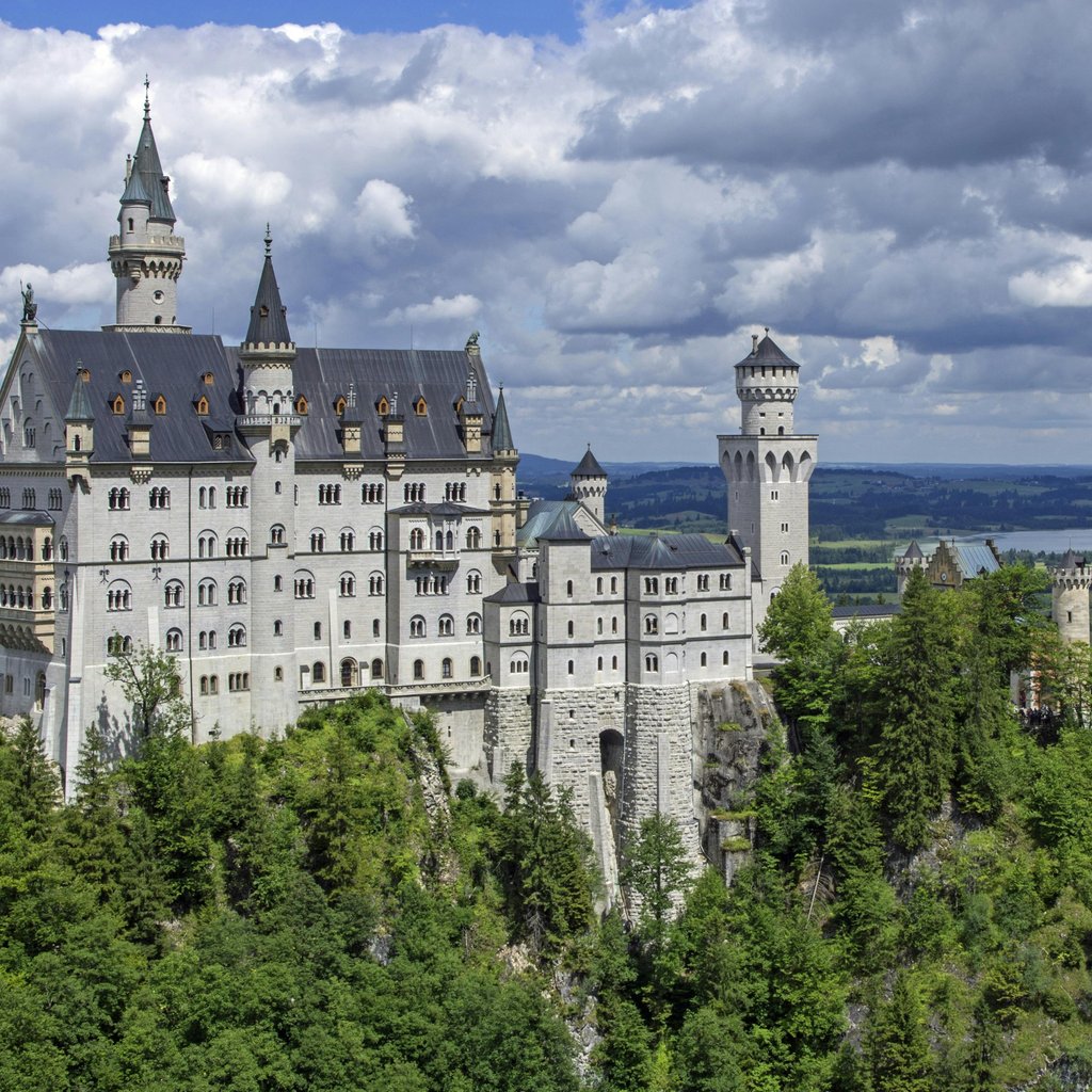 Stunning view of Neuschwanstein Castle surrounded by lush green forests and clouds.