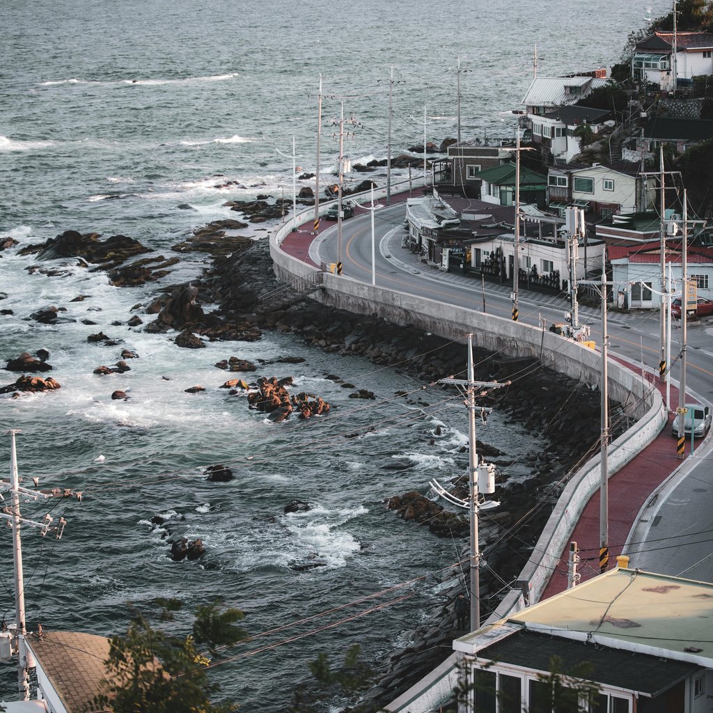 Aerial view of a coastal road and town in Gangneung, South Korea, showcasing seaside urban landscape.