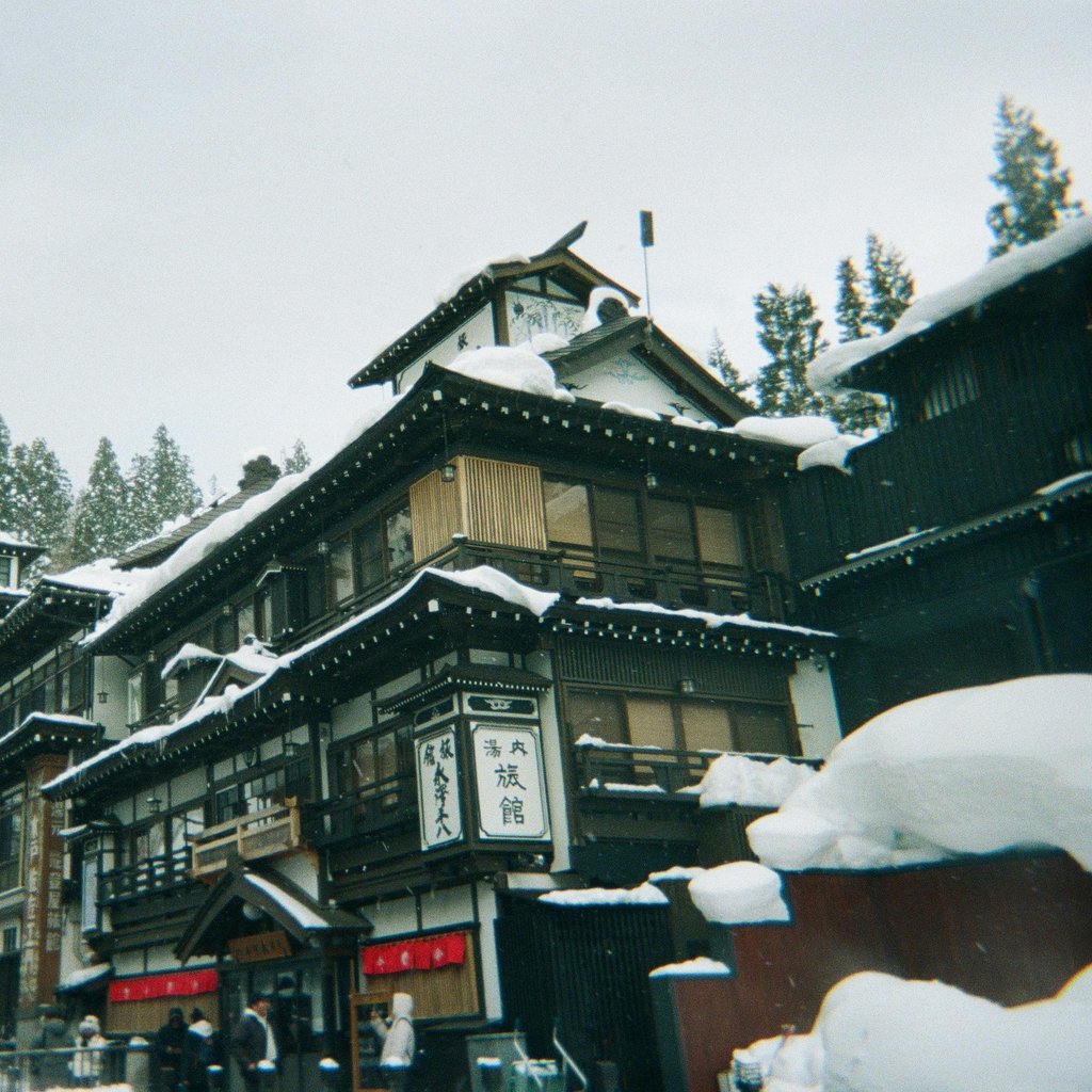 A picturesque view of traditional Japanese architecture in a snowy onsen town, set against a backdrop of snow-covered trees.