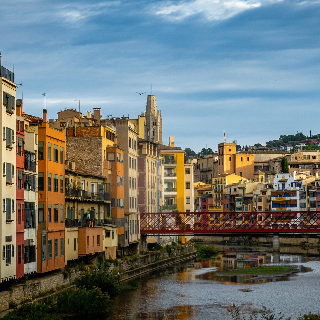 Vibrant cityscape of Girona, featuring colorful riverside buildings and Eiffel Bridge.