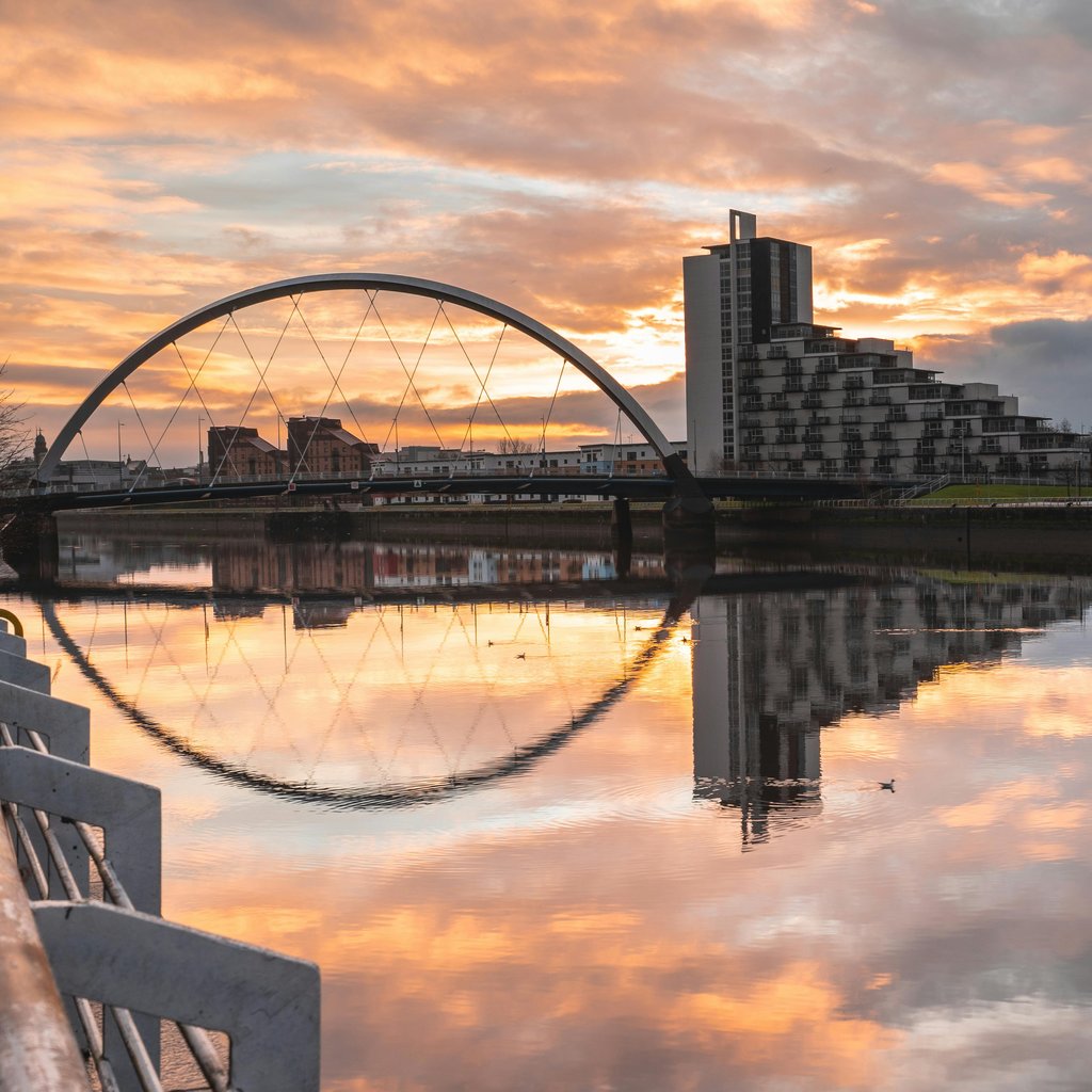 Stunning view of Glasgow's Clyde Arc reflecting in the River Clyde at sunset with modern architecture.
