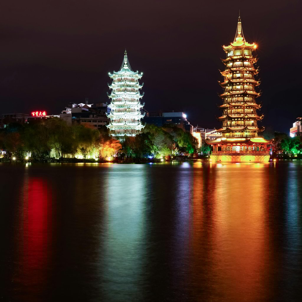 A stunning night view of the illuminated Sun and Moon Pagodas reflecting in a serene river in Guilin, China.