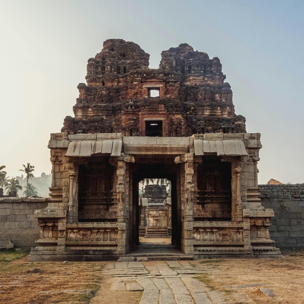 Majestic ancient temple ruins in Hampi, India, captured at sunrise with palm trees in the background.