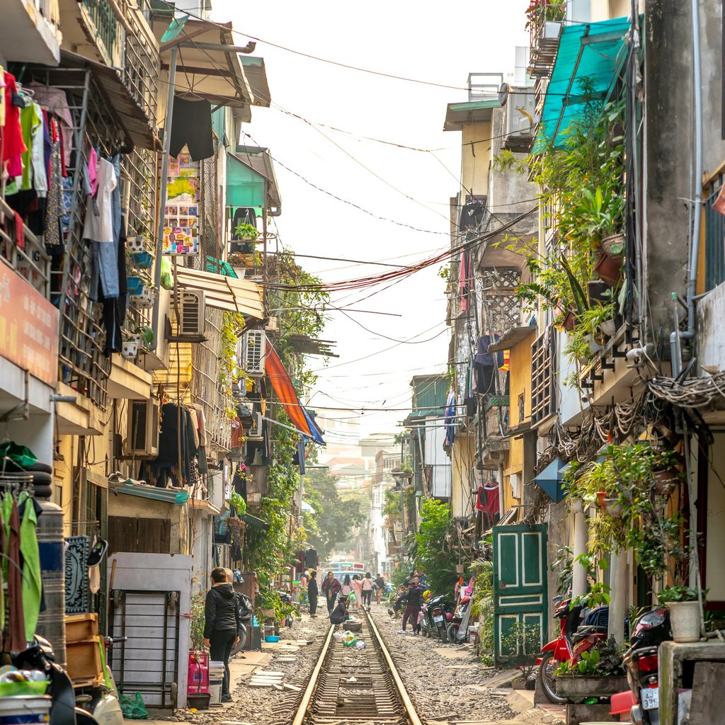 Lively view of Hanoi's famous Train Street with train tracks running between apartment buildings and bustling daily life.
