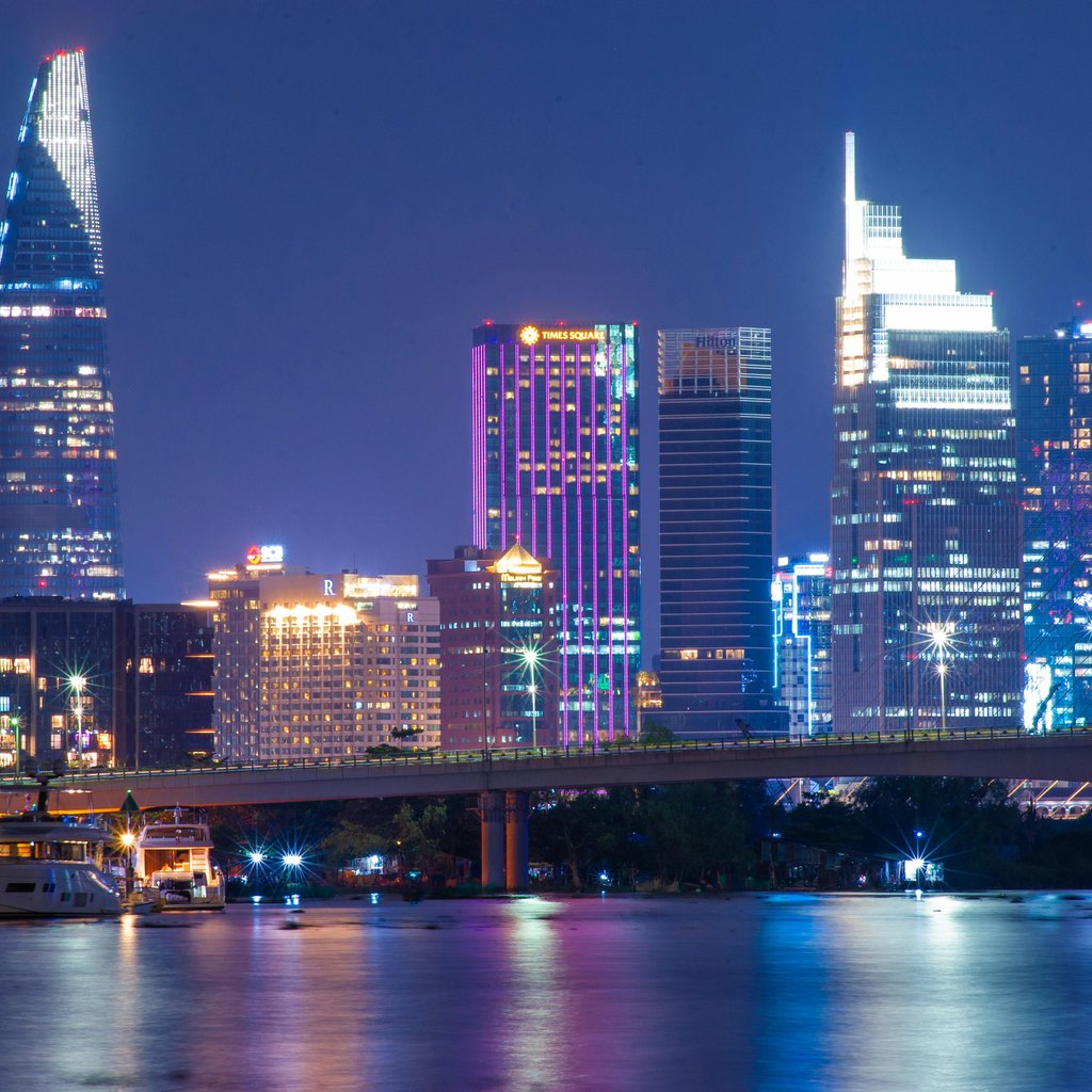Illuminated Ho Chi Minh City skyline with vibrant lights reflecting on the river at night.