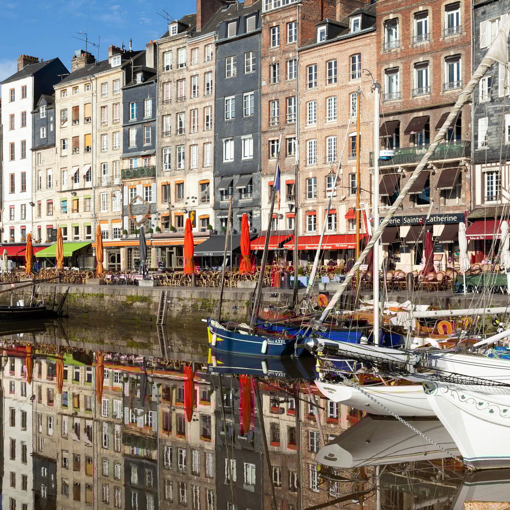 Colorful medieval buildings reflect on the waters of Honfleur Marina in Normandy, France.