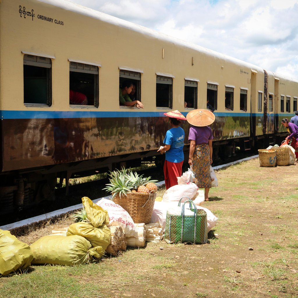 Vendors and villagers exchange goods near a train in Hsipaw, showcasing Myanmar's rural market life.