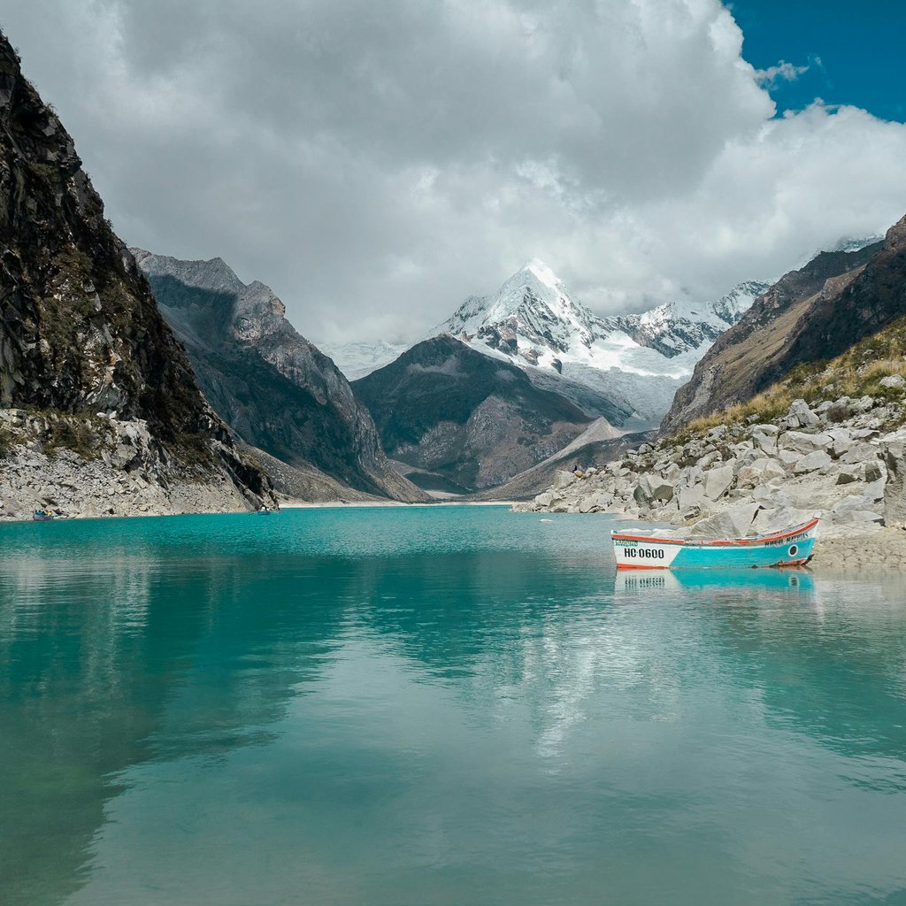 Stunning turquoise lake surrounded by mountains in Huaraz, Peru on a crisp day with a lonely boat.