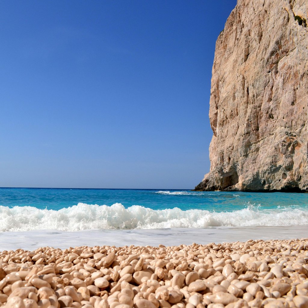 A peaceful seashore scene with a boat near a cliff and turquoise waters under a clear sky.