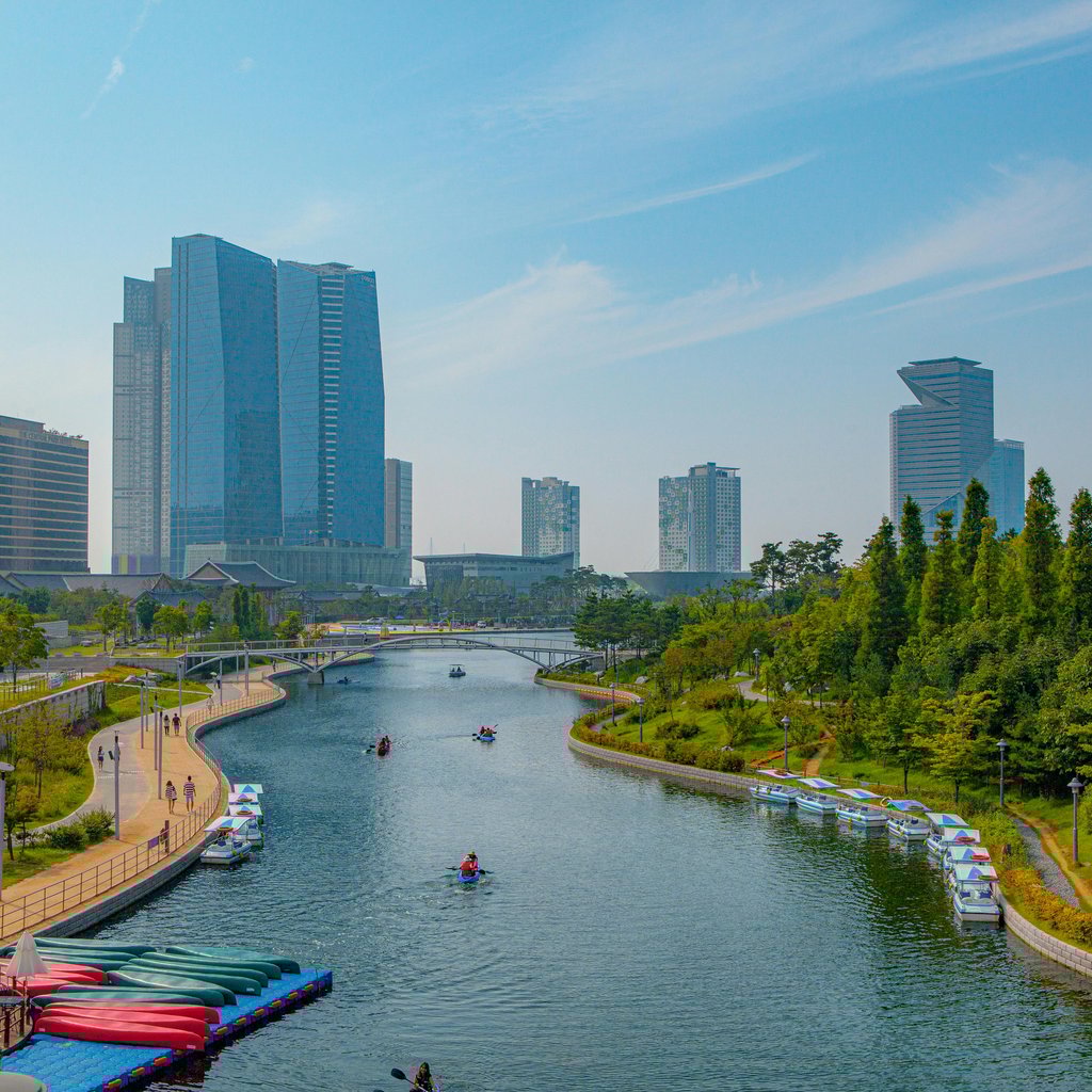 A scenic view of a modern urban skyline with a river flowing through a park in Incheon, South Korea.