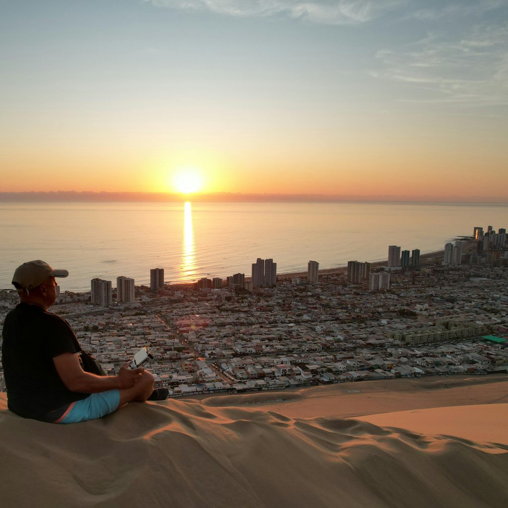 A serene view of Iquique from a sand dune overlooking the cityscape at sunset.