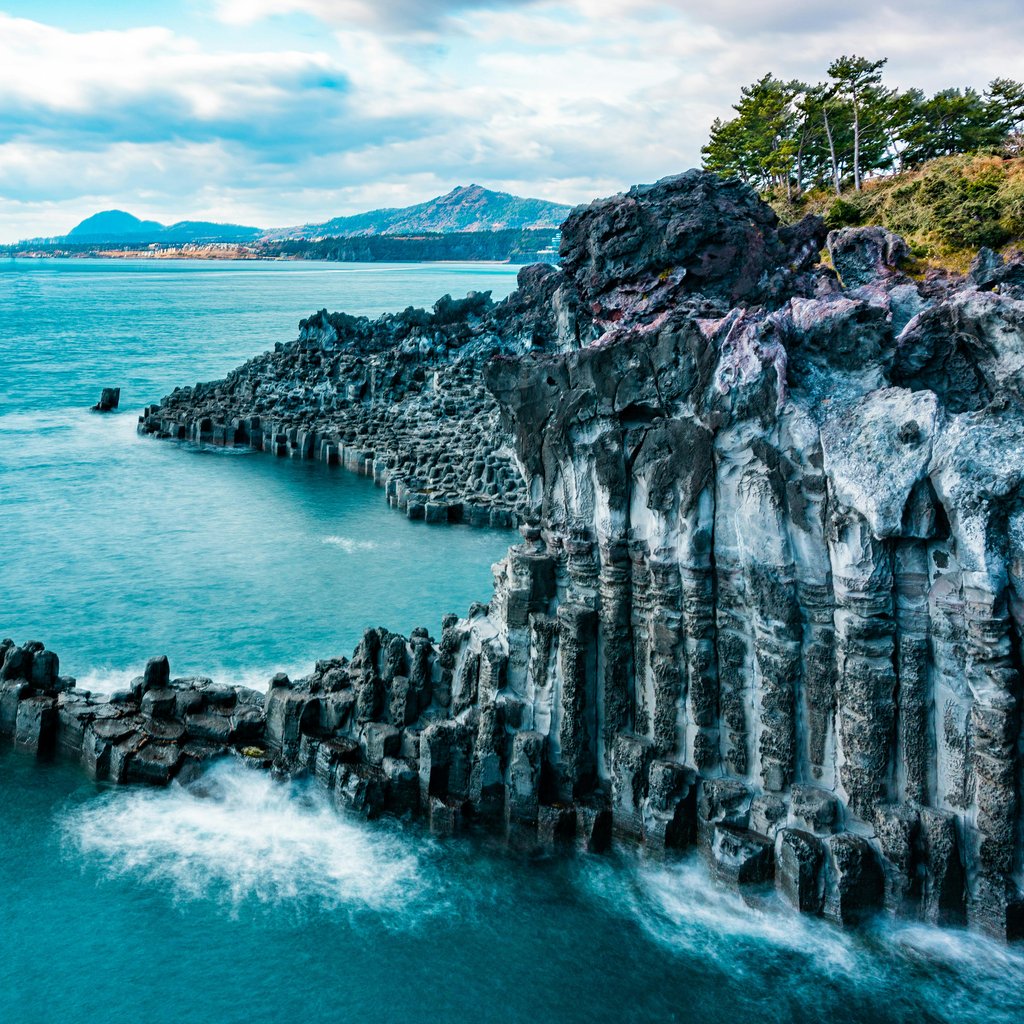 A breathtaking view of Jeju's volcanic cliffs with turquoise waters and dramatic scenery.