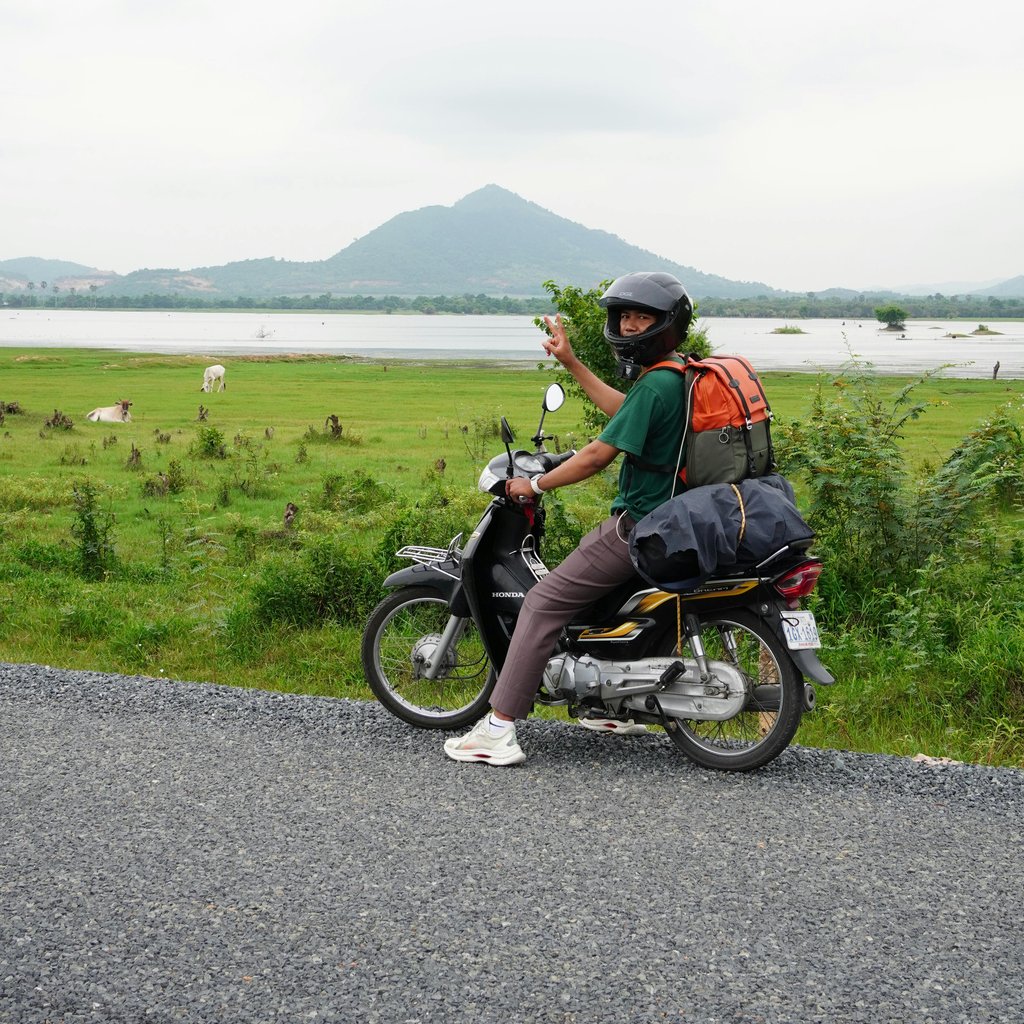 A traveler rides a motorbike through the scenic countryside of Kampot, Cambodia, enjoying an outdoor adventure.
