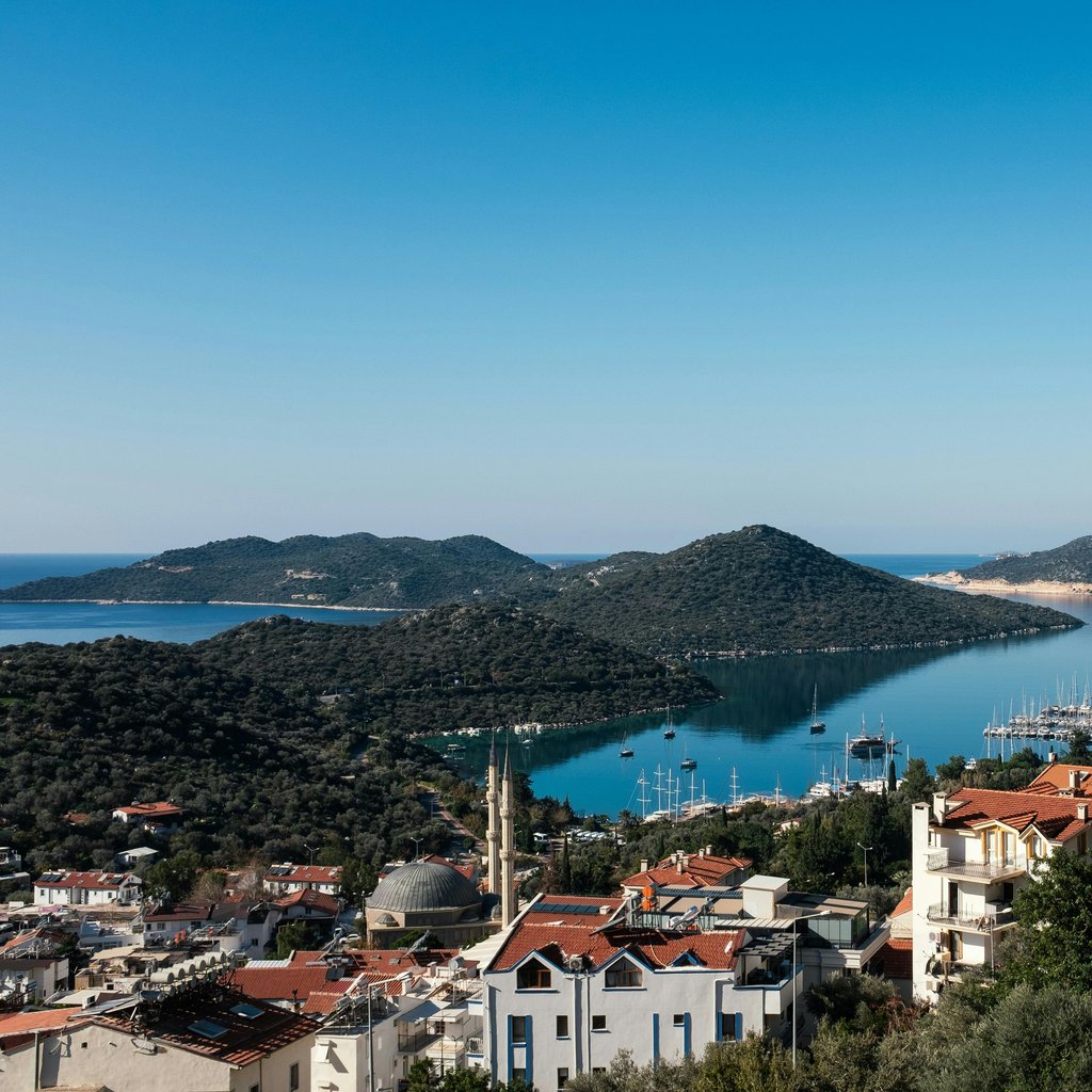 A stunning aerial view of Kas harbor, Antalya with clear skies, blue sea, and surrounding hills.