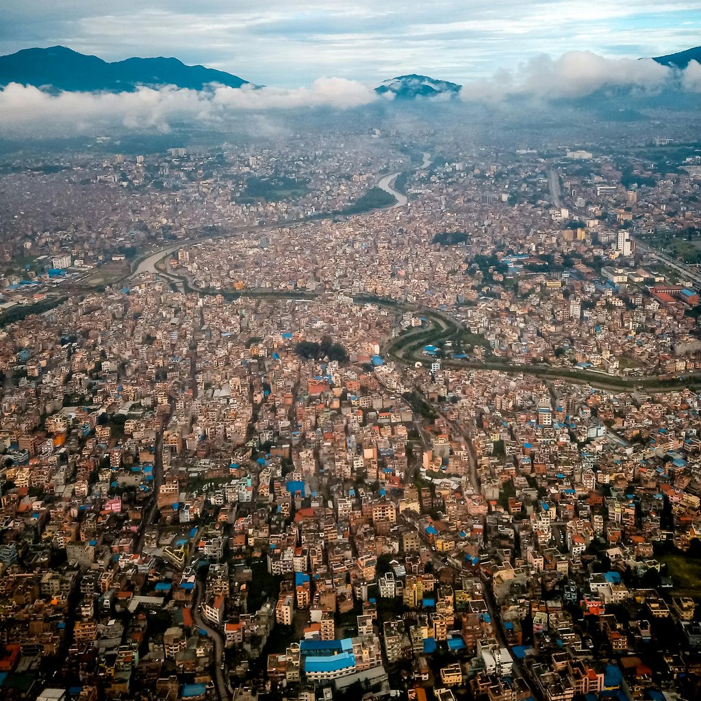 Stunning aerial view of Kathmandu cityscape surrounded by mountains and clouds.