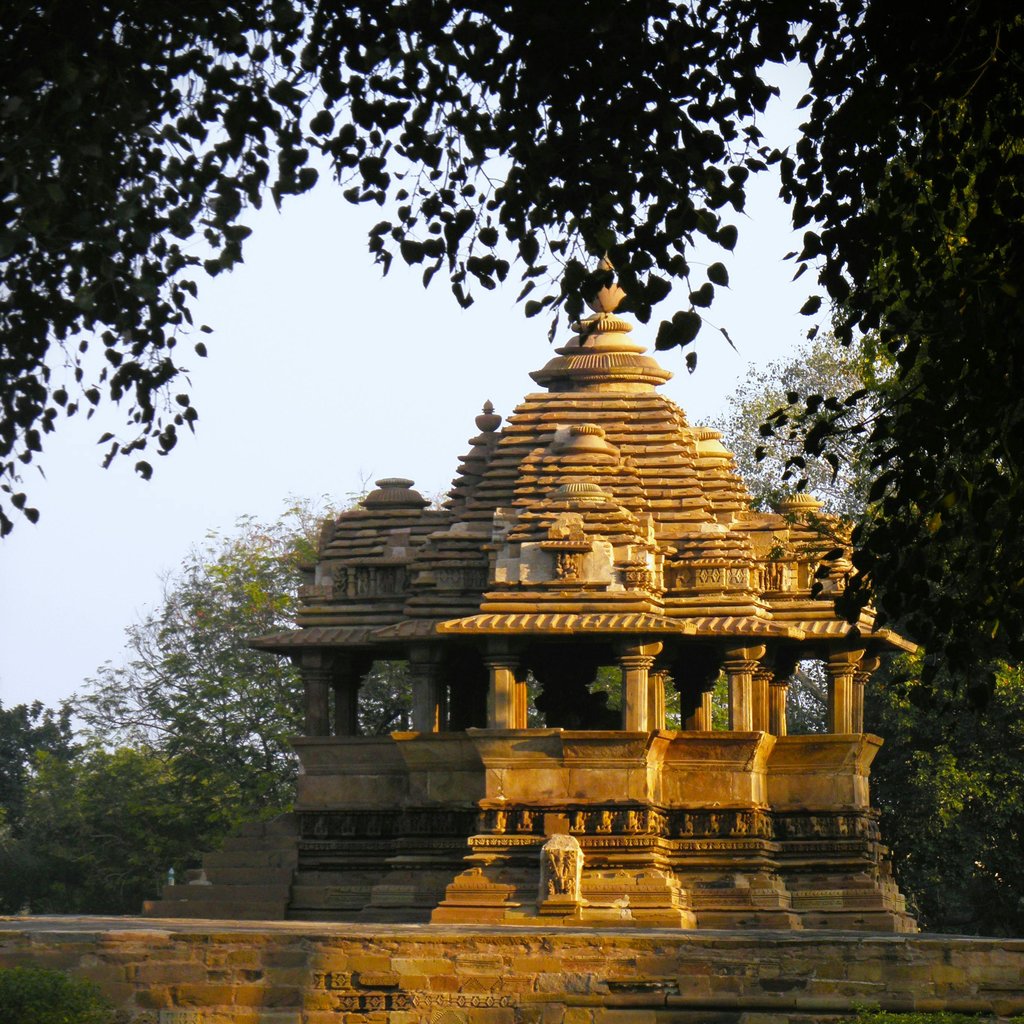 View of a historic Khajuraho temple surrounded by lush greenery in Madhya Pradesh, India.