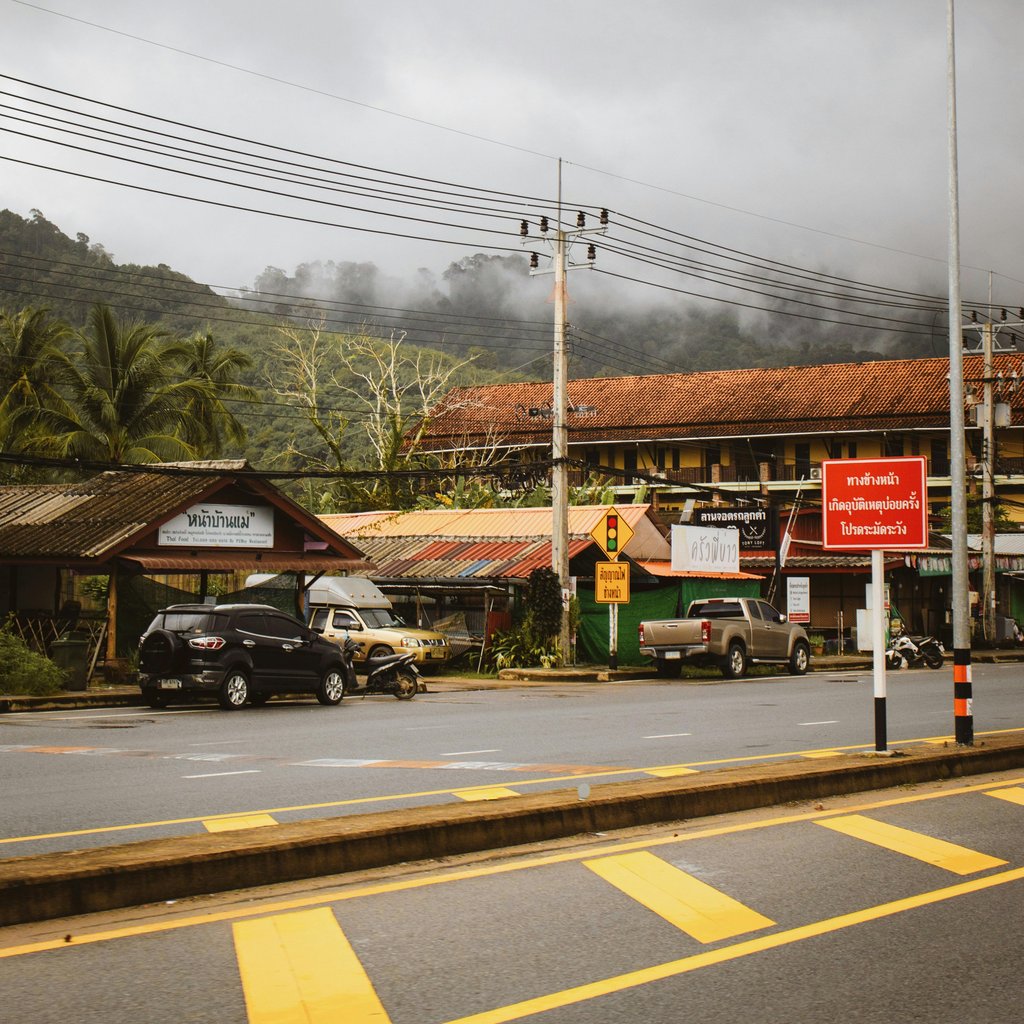 A bustling street view in Khao Lak, Thailand, showcasing local architecture under cloudy skies.