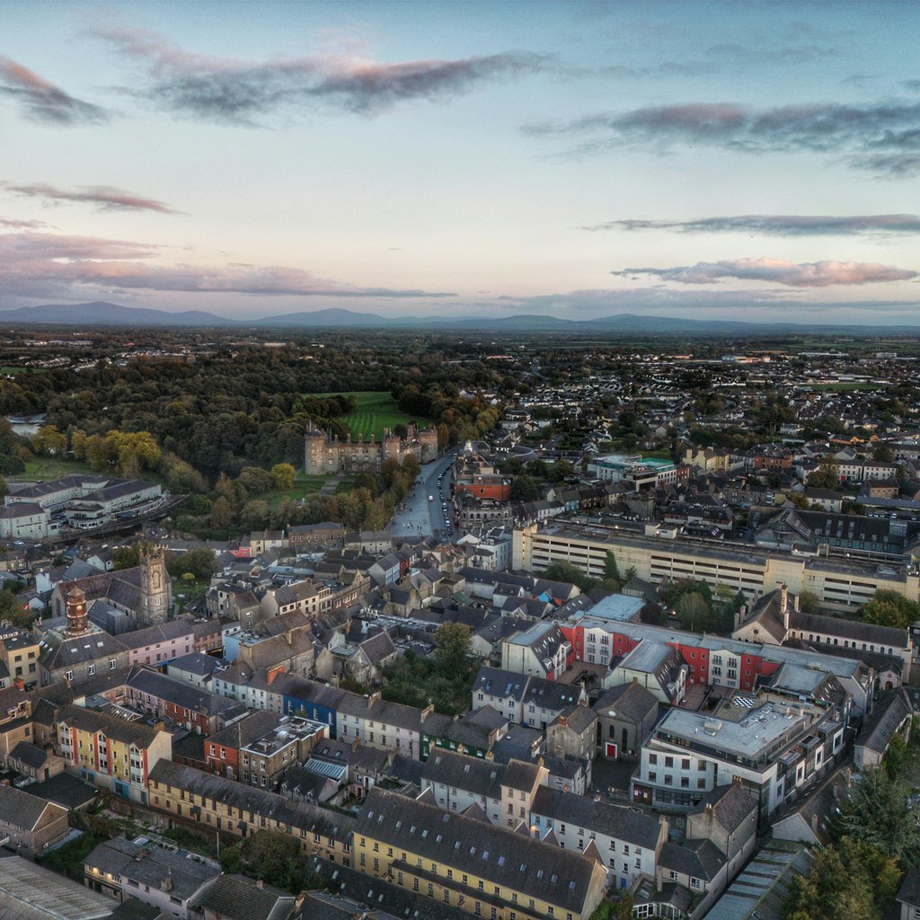 Stunning aerial view of Kilkenny cityscape with Kilkenny Castle at dusk, showcasing residential areas and lush greenery.