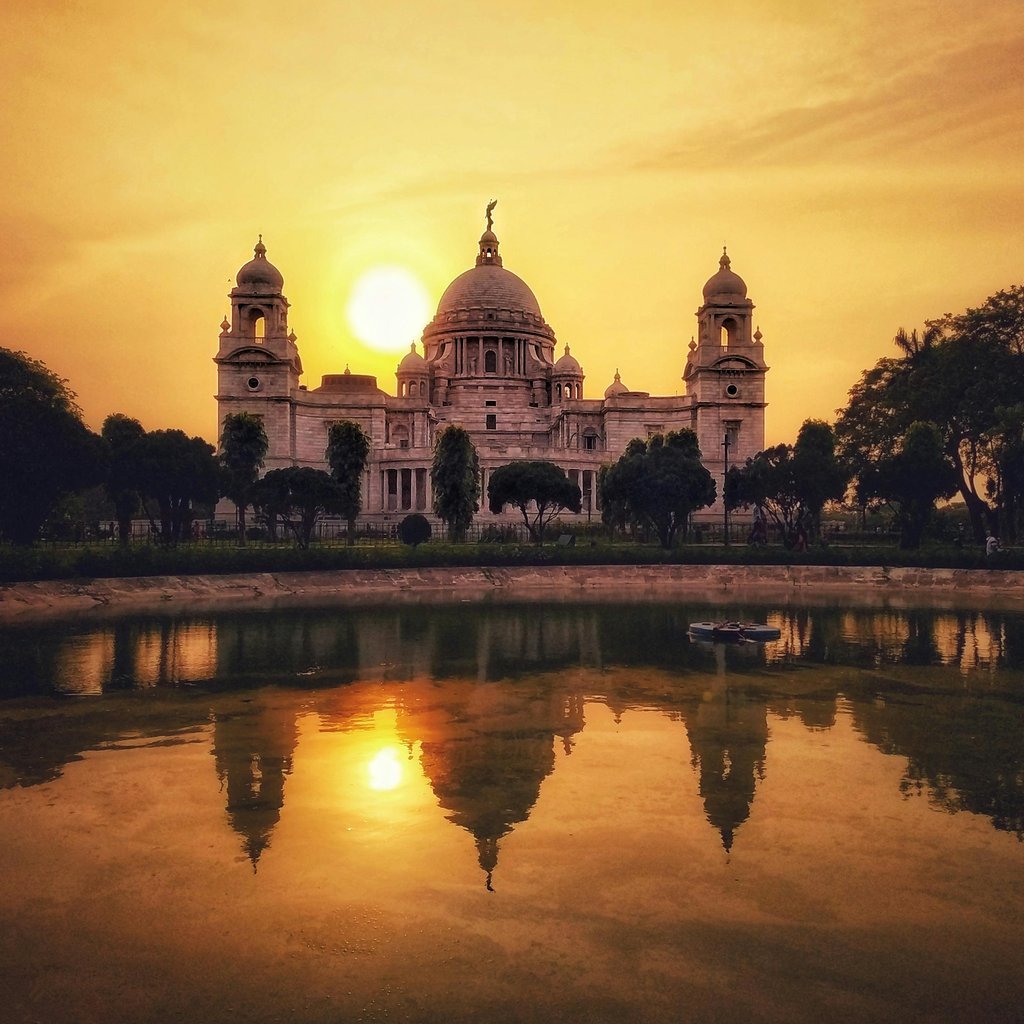 Captivating view of Victoria Memorial with sunset reflection on tranquil water in Kolkata, India.
