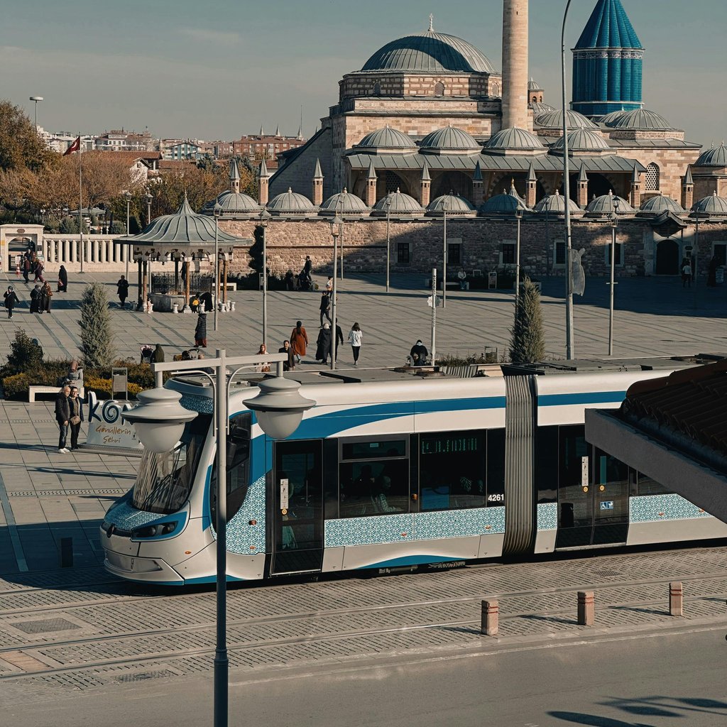 A modern tram moving past the historic Mevlana Museum in Konya, Turkey under clear skies.